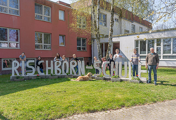 Schüler und Mitarbeitende mit Schulhund vor Buchstaben Rischborn‑Schule